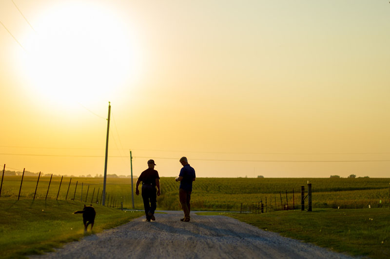 An old farmer and young farmer on a dirt road at sunset