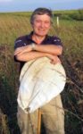 Jerry DeWitt standing in a field smiling at the camera holding a white bag