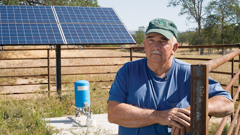 Man posing with solar panels and a water pump on his property