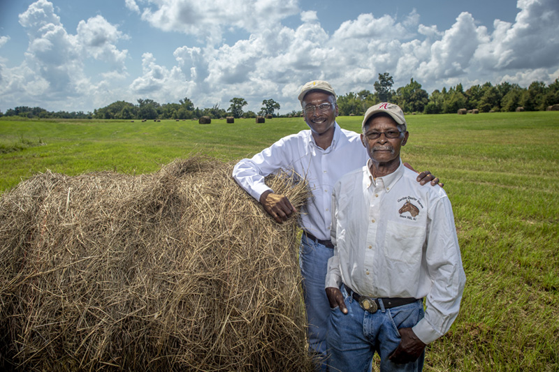 A middle aged farmer and his father posing next to a hay bale