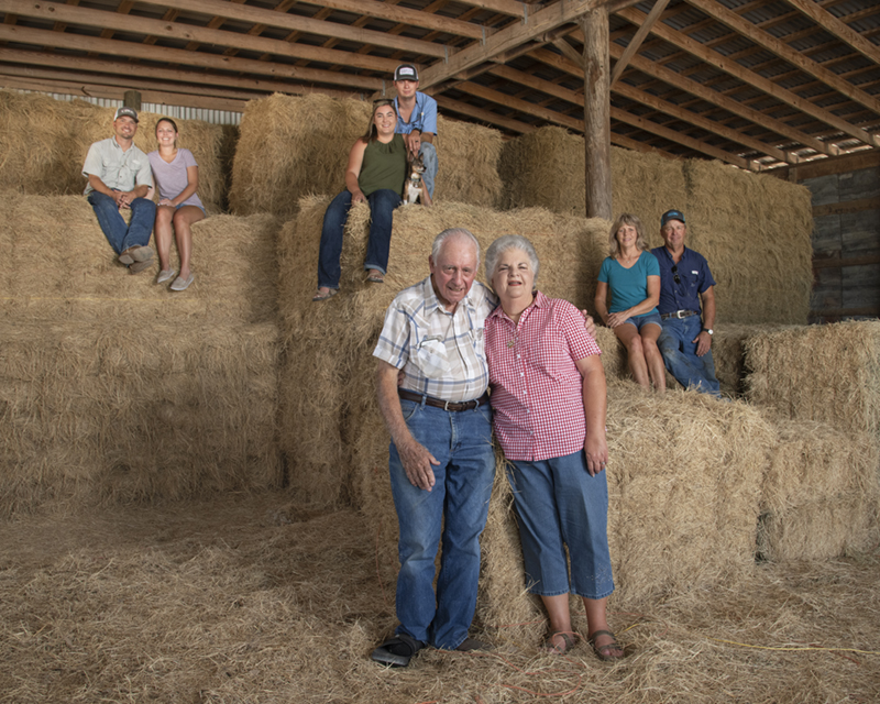 Three adult generations of a farm family pose in a hay barn