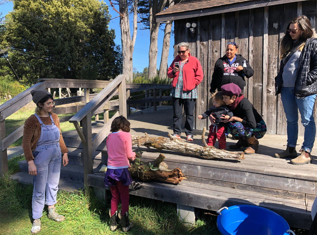 Person sits on porch and teachers others how to inoculate a mushroom log. 