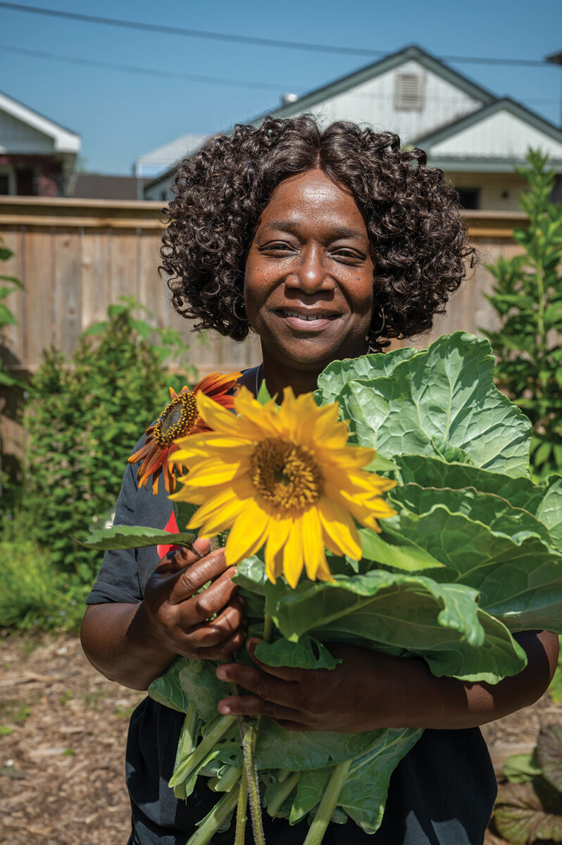 Woman holding a yellow sunflower outside in a fenced garden