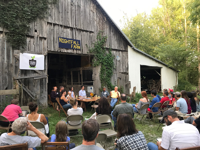 A group sits during a presentation with a barn in the background