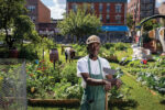 a man poses with a hoe in front of his urban farm