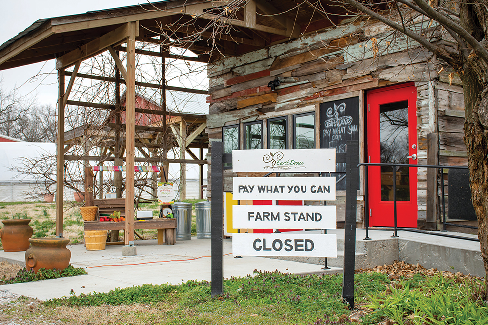 A wooden house with a red door, with a sign advertising the Farm Stand