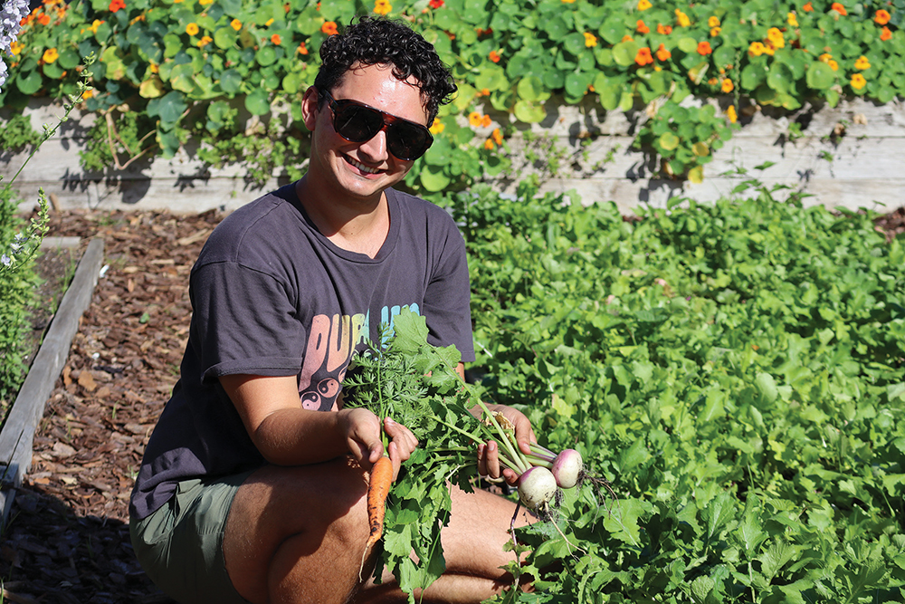 a person kneels and poses with harvested radishes