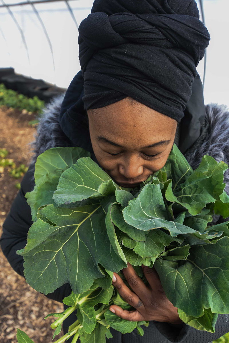 A young woman is hugging a bunch of collards with a look of satisfaction