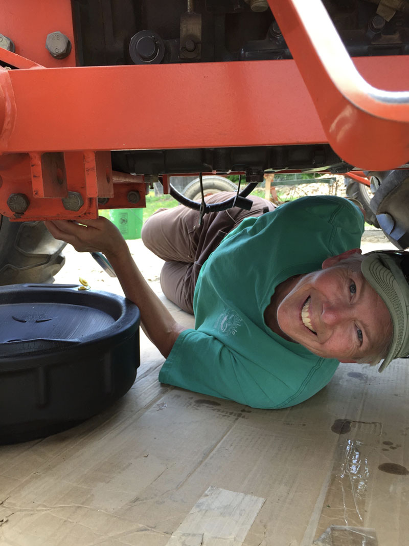 A woman is posing while lying under a tractor and changing the oil